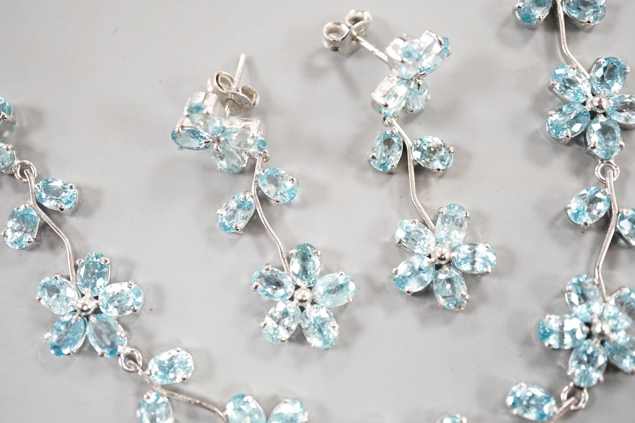 A modern 925 and blue zircon suite of jewellery, comprising a flower head cluster necklace and a pair of matching earrings.